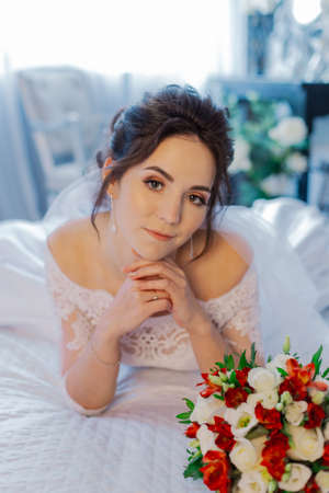 Beautiful happy bride on the bed with a wedding bouquet.の写真素材