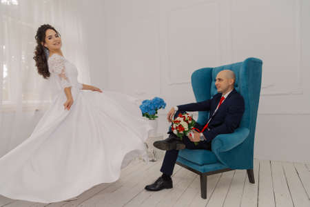 A handsome groom is sitting on a chair. The bride shows him his dress.の写真素材