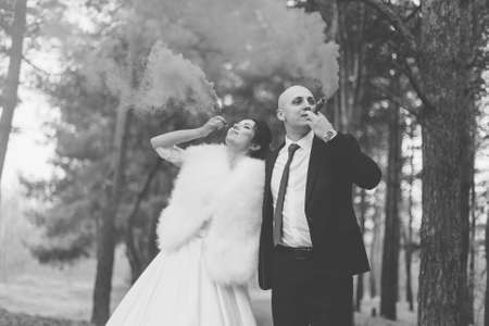 Happy bride and groom hold colored smoke in their hands.の写真素材