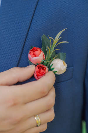 Stylish young groom straightens a boutonniere on a jacket.