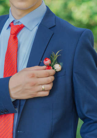 Stylish young groom straightens a boutonniere on a jacket.