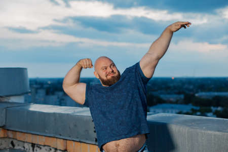 Big bearded bodybuilder on the rooftop in the evening.