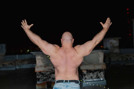 Big bearded bodybuilder on the rooftop in the evening.
