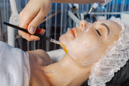 Professional beautician woman applies a mask with a brush to her neck.の写真素材