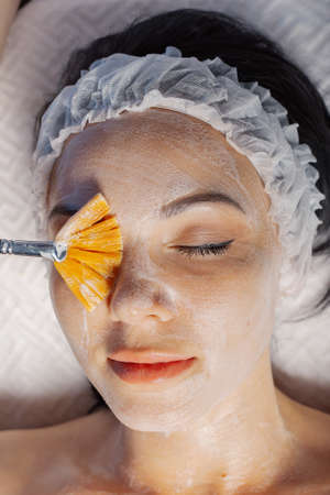 Professional beautician woman applies mask with brush to clients face.