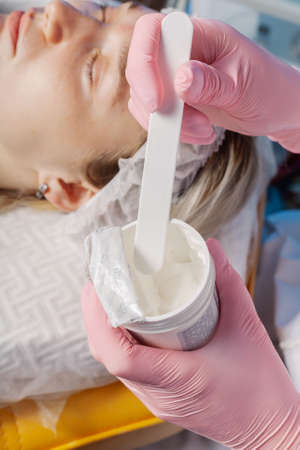 A professional beautician picks up the cream with a spatula from a jar.の写真素材