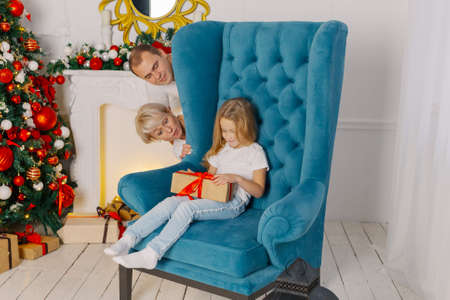 Beautiful young happy and cheerful family on an armchair near the New Year tree.