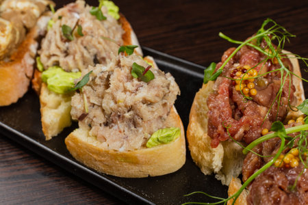 Three types of bruschetta on the table on a black plate beautiful serving in a restaurant. classic snack. close-up of fish and meat bruschettaの写真素材