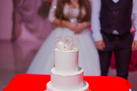 A beautiful handmade wedding cake you stands on a table with a red tablecloth. two hearts on top of the cakeの写真素材