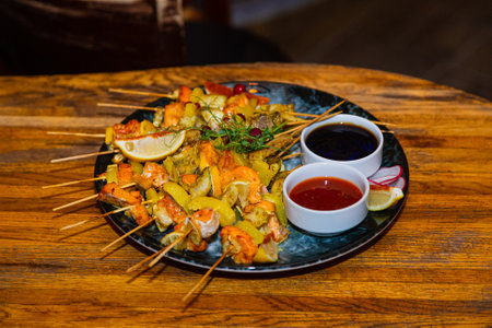 Shish kebab from seafood and red fish on wooden skewers on a plate with sauces on a wooden table. general plan side viewの写真素材