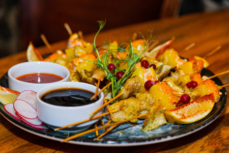 Shish kebab from seafood and red fish on wooden skewers on a plate with sauces on a wooden table. close-up of delicious food.の写真素材