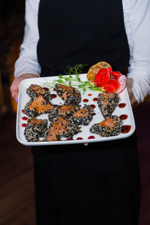 Grilled red fish meat with sesame seeds in the hands of the waiter. Plate with fish and ginger