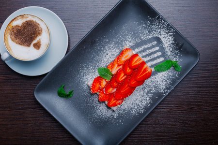 Appetizing dessert on a plate with fresh strawberries and a cup of cappuccino.sweet dessert. fresh mint. view from aboveの写真素材