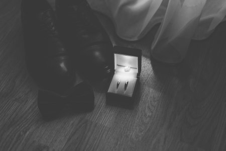 The groom's new black shoes on the floor near a white curtain with a butterfly and rings on the wedding day. Black and white photographyの写真素材