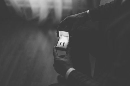A young groom on his wedding day holds wedding gold rings in his hands, he is very happy. box for rings with illumination. black and white photoの写真素材