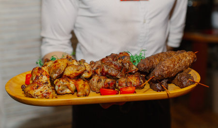 Shish kebab from different types of meat lies on a tray held by a young waiter in a restaurantの写真素材