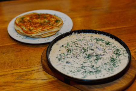 Fresh fried pancakes on a plate and gravy in a pan with sour cream herbs and mushroomsの写真素材