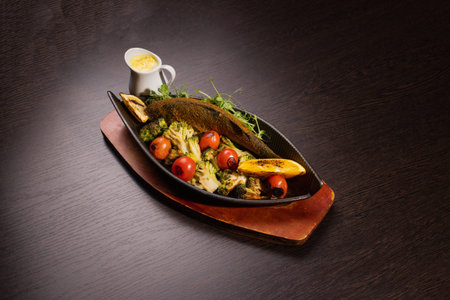 Baked fish with vegetables and sauce in a plate on a wooden tray