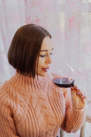 Beautiful young girl sitting at a table in a restaurant with a glass of red wine and posing