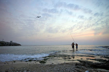 Beirut - Lebanon, October 12, 2008: Sunset coastal view at Raouche bay in Beirut showing two fishing men and an approaching airplane.のeditorial素材