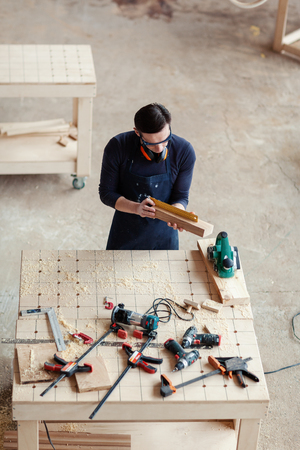 From above young woodworker measuring wooden plank with ruler at workbench covered with tools and sawdustの写真素材