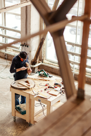 From above young woodworker measuring wooden plank with vernier caliper tool at workbenchの写真素材