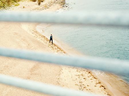 High angle through railing view of young athlete jogging alone on beach along sea shoreの写真素材