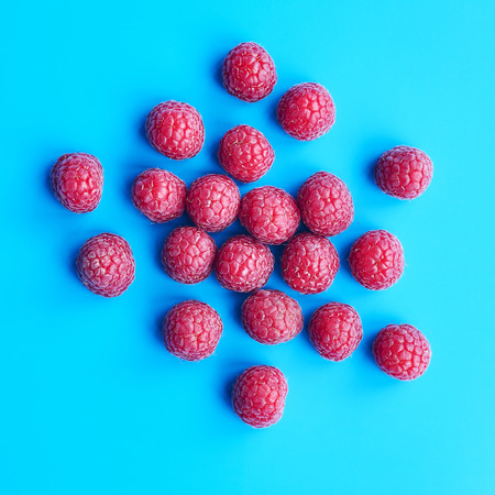 Top view squared flatlay with pile of ripe juicy raspberries on blue, sweet vegan dessertの写真素材