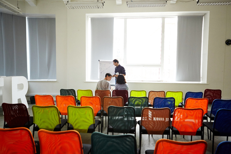 Back view of two colleagues sitting on chairs in conference hall and listening to man making presentationの写真素材