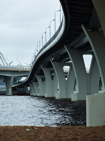 View of two modern bridges crossing over surface of rippling water on gray dayの写真素材