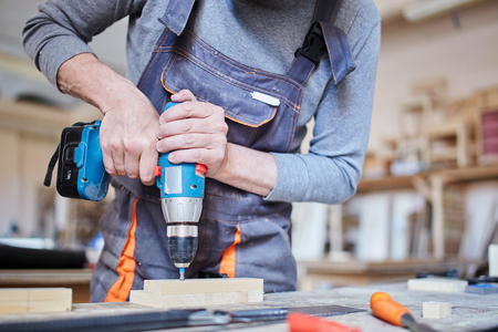 Crop shot of adult carpenter in overall drilling holes in plank of wood working on piece of furnitureの写真素材