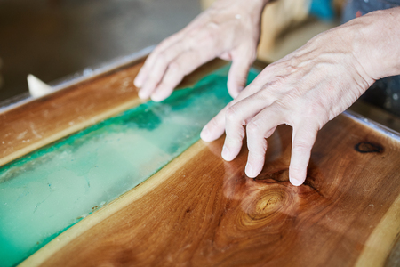 Crop hands of carpenter working on beautiful table top with blue epoxy resin elementの写真素材