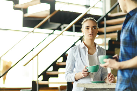 Girl standing at counter with coffee cup and chatting with anonymous man in cafeteriaの写真素材