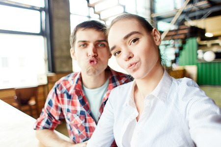 Expressive young girl and boy making faces at camera taking selfie and having fun togetherの写真素材