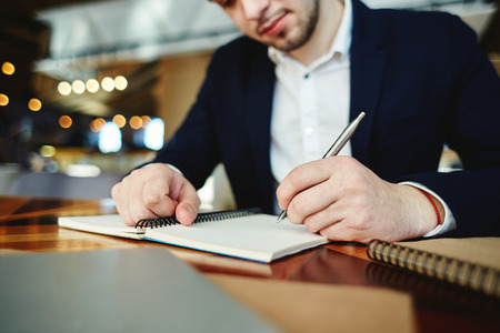 Cropped businessman in formalwear writing in his notebook while sitting at table in cafeの写真素材