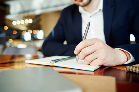 Unrecognizable businessman holding pen in his hand and thinking over notes in his notebookの写真素材