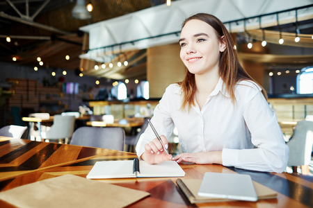 Portrait of confident businesswoman smiling while thinking of plans at cafe tableの写真素材