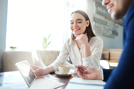 Cheerful businesswoman holding tablet computer and showing data on screen to her male collague. Business partners having coffee meeting at cafeの写真素材