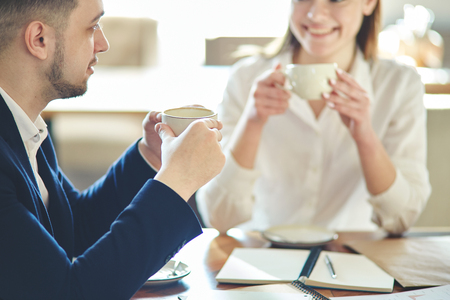 Businessman wearing white shirt and jacket talking to defocused female business partner during meeting in cafe. Business people drinking coffee and having friendly discussionの写真素材