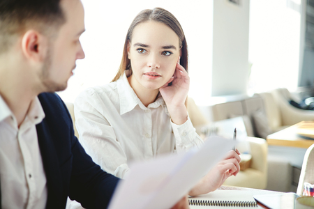 Business partners planning strategy at meeting. Businesswoman asking questions to male colleague holding documentsの写真素材