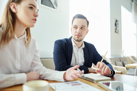 Two business partners discussing report with financial stats at meeting; businessman listening to his female colleagueの写真素材