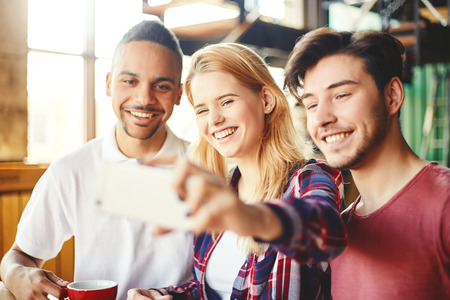Portrait of three multi-ethnic college students having fun while taking selfie with smartphone...
