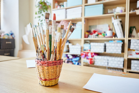 Basket with collection of various paint brushes placed on table in classroom in art schoolの写真素材