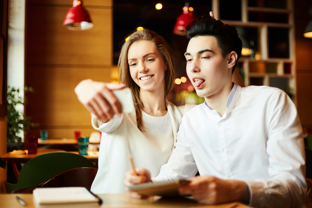 Playful  young man and woman having fun while taking selfie together in cafe over studiesの写真素材