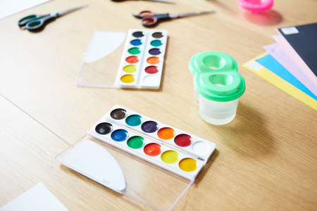 From above shot of boxes with watercolors and plastic non spill water cup placed on desk in art school classroomの写真素材