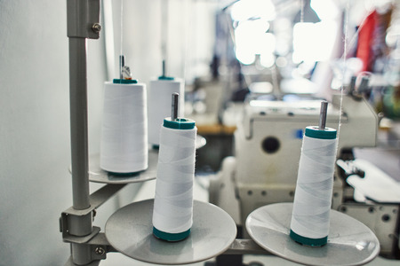 Close-up spools with thin white thread attached to metal holder in tailor workshop