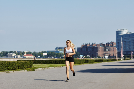 Beautiful young female running fast towards camera on asphalt path during outdoor workout on sunny dayの写真素材