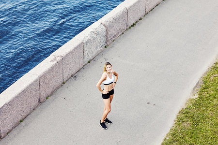 From above shot of young female in sportswear smiling and looking at camera while standing on asphalt path near riverの写真素材