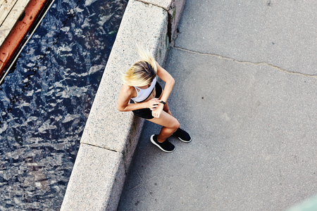 From above shot of unrecognizable female in sportswear leaning on border near river and looking at data on fitness tracker screenの写真素材