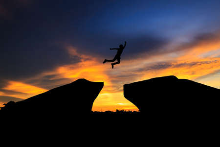 Man jump through the gap between hill.man jumping over cliff on sunset background,Business concept ideasundown; sunrise; sunset; thailand; water; winterの写真素材